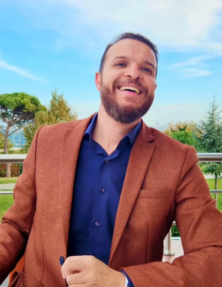 Mohammed Mansour smiling outdoors in a brown jacket