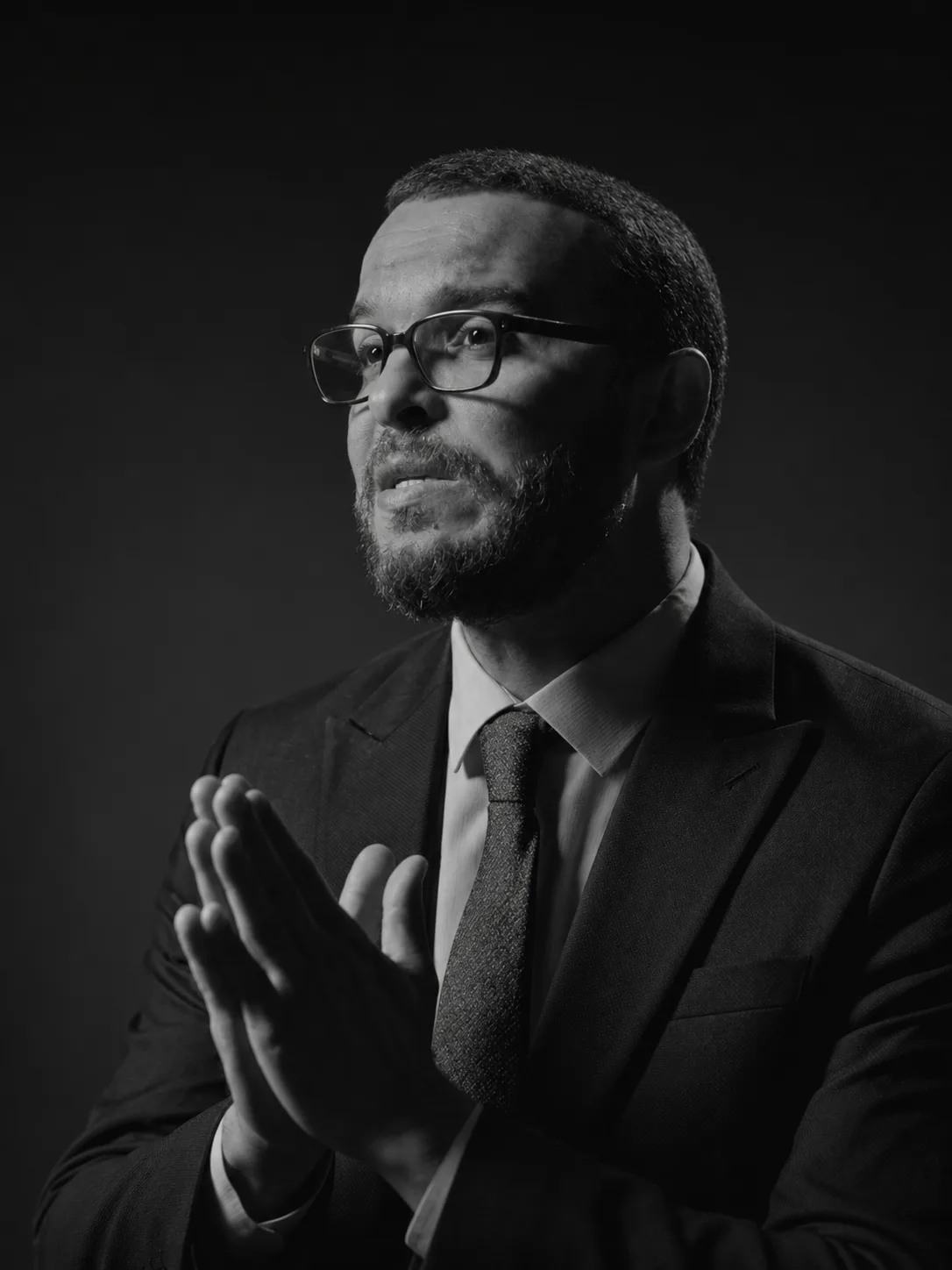 Mohammed Mansour wearing glasses, hands held together as he speaks